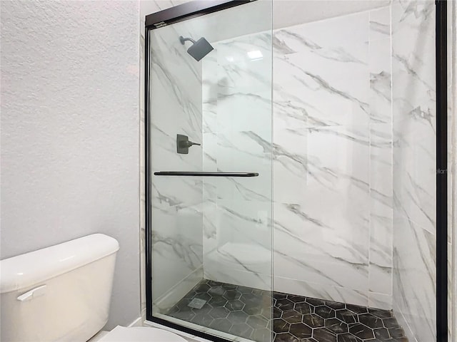 bathroom featuring a shower with door and toilet