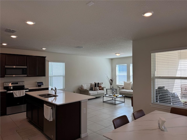 kitchen with a textured ceiling, light tile patterned flooring, sink, a center island with sink, and appliances with stainless steel finishes