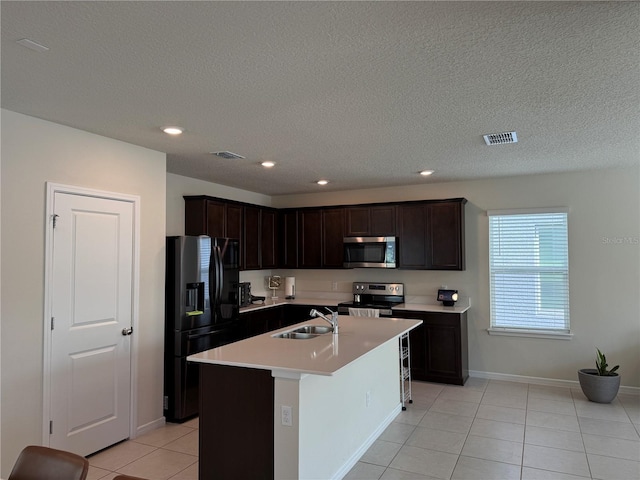 kitchen with a textured ceiling, light tile patterned flooring, a kitchen island with sink, sink, and appliances with stainless steel finishes