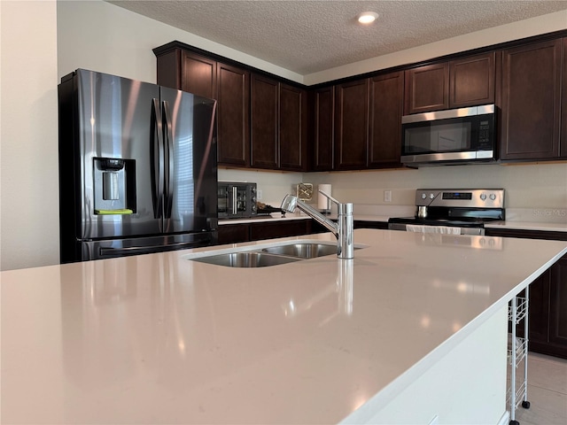 kitchen with appliances with stainless steel finishes, an island with sink, a textured ceiling, dark brown cabinetry, and sink