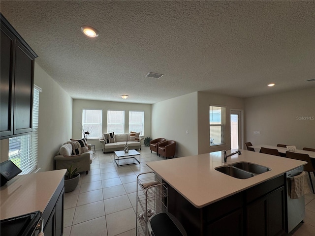 kitchen with light tile patterned flooring, dishwasher, a textured ceiling, a center island with sink, and sink