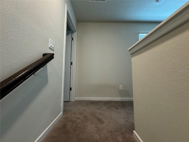 hall with a textured ceiling and dark colored carpet