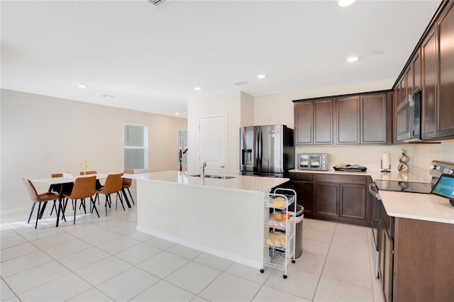 kitchen featuring appliances with stainless steel finishes, an island with sink, sink, light tile patterned floors, and dark brown cabinetry