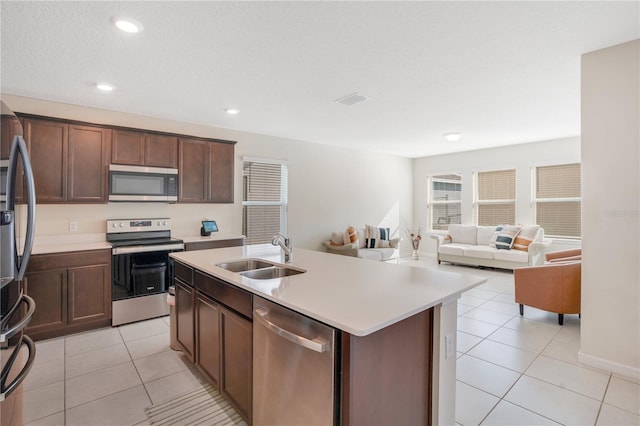 kitchen featuring dark brown cabinetry, sink, a center island with sink, light tile patterned floors, and stainless steel appliances