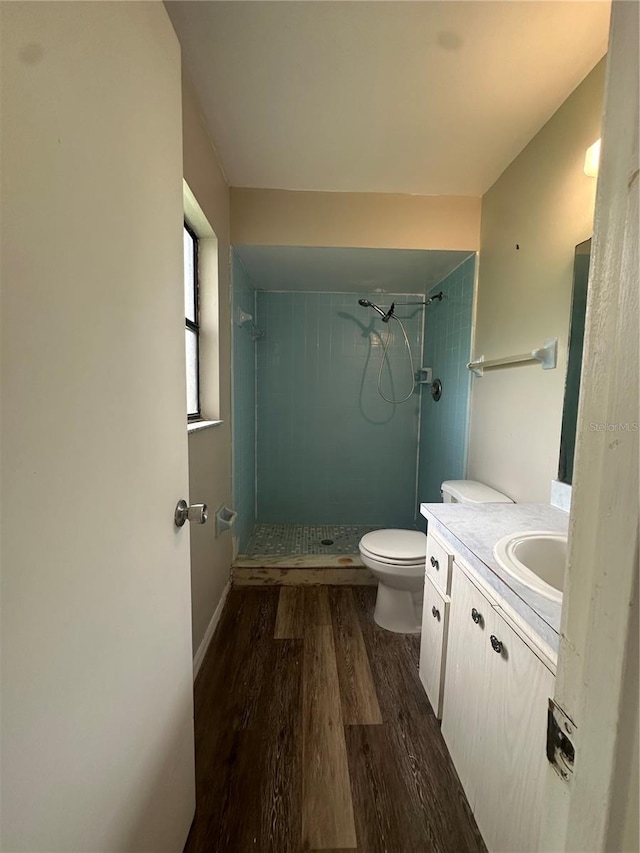 bathroom with a tile shower, hardwood / wood-style floors, vanity, and toilet