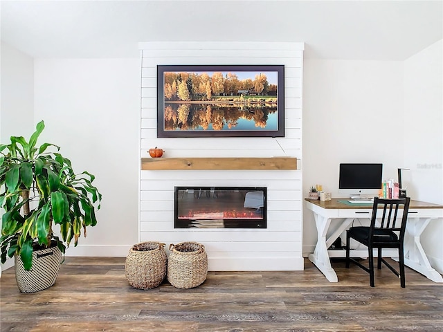 home office with a large fireplace and dark wood-type flooring