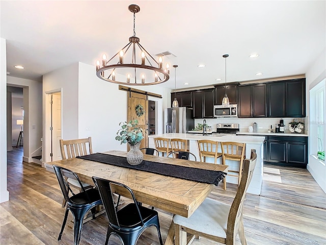 dining room with a barn door, light hardwood / wood-style floors, sink, and a chandelier