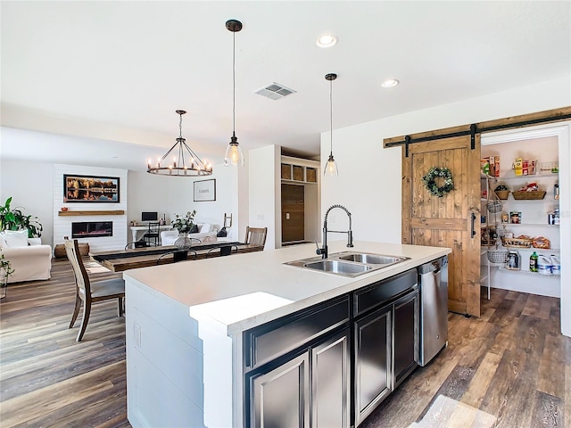 kitchen featuring a barn door, dishwasher, decorative light fixtures, a center island with sink, and sink