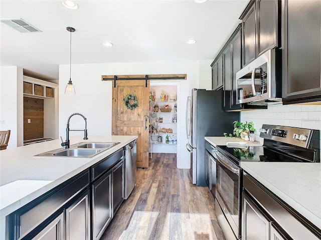 kitchen with hanging light fixtures, sink, stainless steel appliances, a barn door, and hardwood / wood-style floors