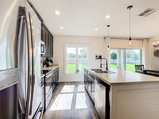 kitchen with an island with sink, tasteful backsplash, pendant lighting, stainless steel appliances, and sink