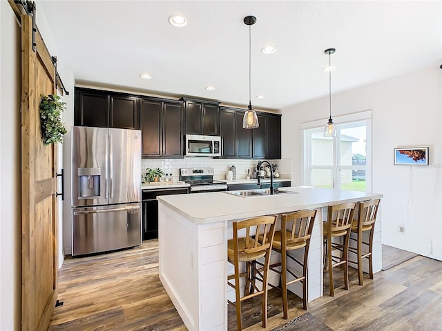 kitchen with hanging light fixtures, an island with sink, a barn door, stainless steel appliances, and sink