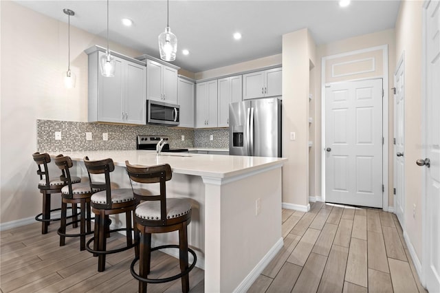 kitchen with pendant lighting, kitchen peninsula, light hardwood / wood-style flooring, stainless steel appliances, and a kitchen bar