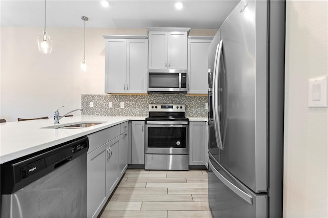 kitchen featuring gray cabinetry, decorative backsplash, stainless steel appliances, decorative light fixtures, and sink