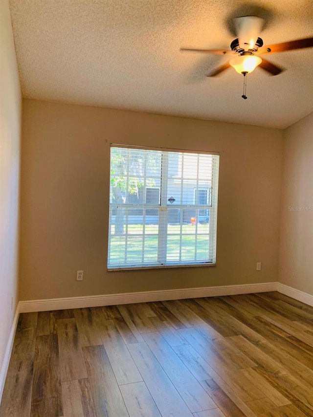 empty room with dark wood-style floors, baseboards, a ceiling fan, and a textured ceiling