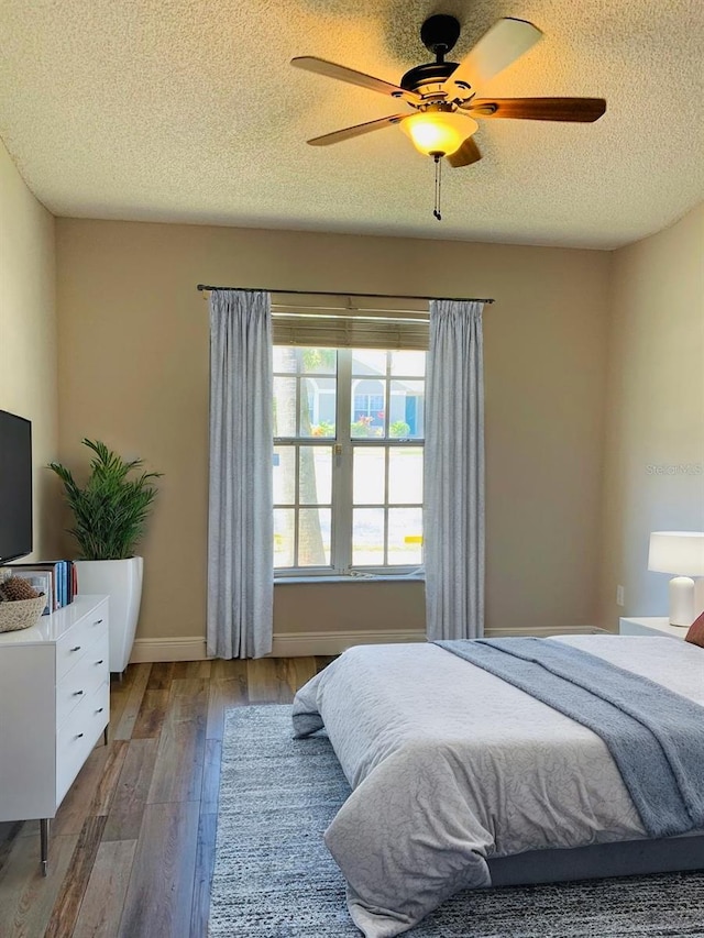 bedroom with a textured ceiling, ceiling fan, wood finished floors, and baseboards