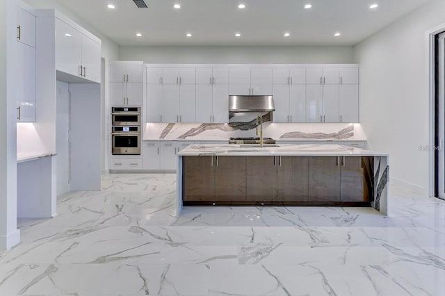 kitchen with a center island with sink, white cabinetry, stainless steel double oven, range hood, and a breakfast bar area