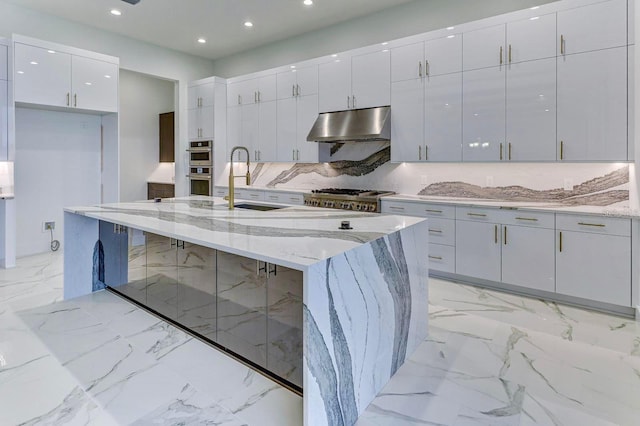 kitchen featuring an island with sink, light stone countertops, white cabinets, sink, and a kitchen breakfast bar