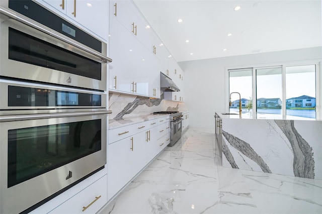 kitchen with appliances with stainless steel finishes, light stone counters, white cabinetry, and sink