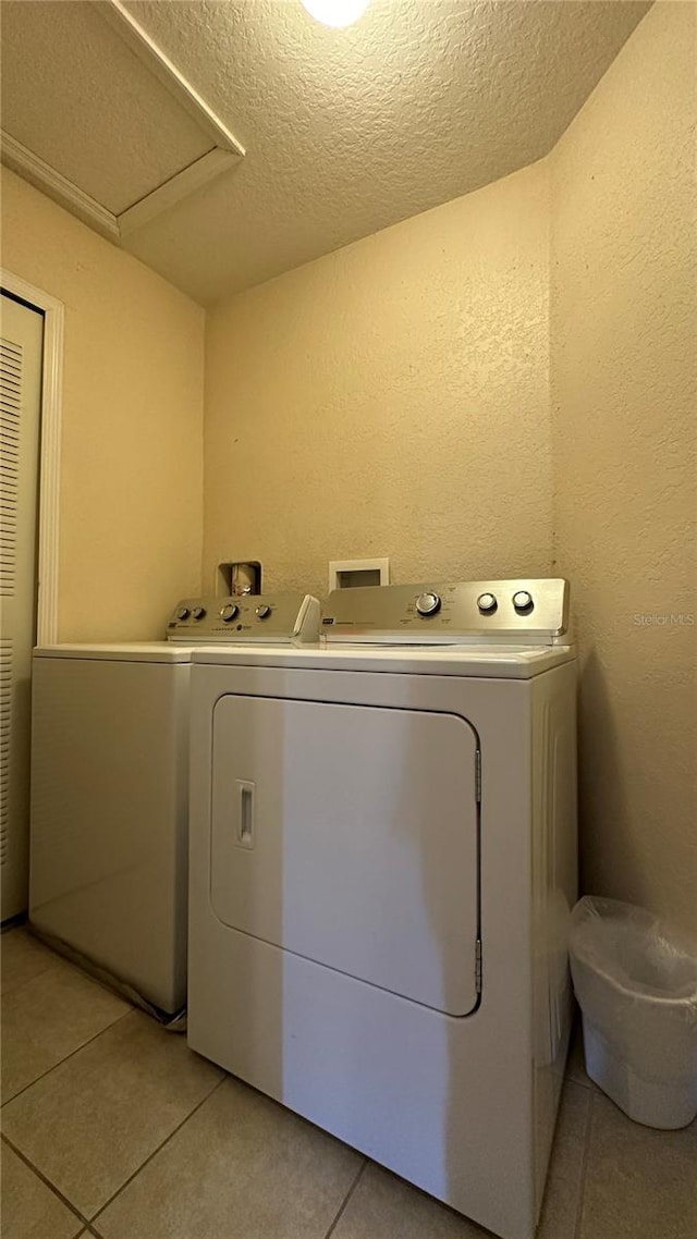 washroom with a textured ceiling, washing machine and dryer, and light tile patterned floors