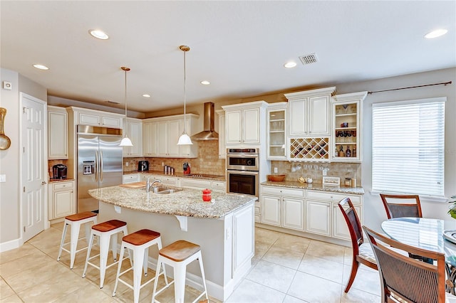 kitchen with pendant lighting, a center island with sink, wall chimney range hood, stainless steel appliances, and decorative backsplash