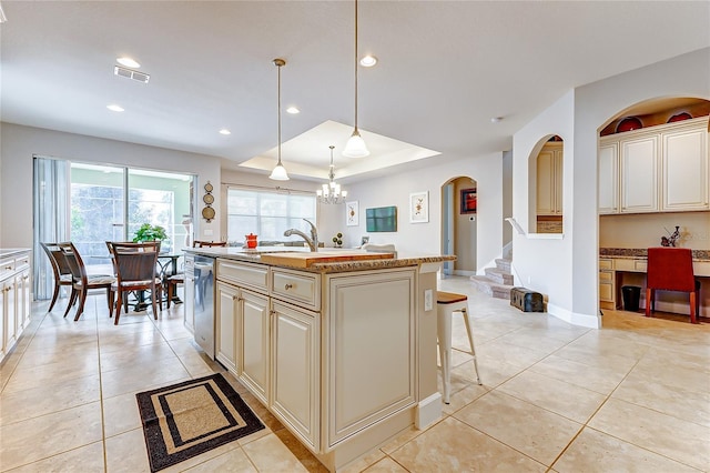 kitchen with an island with sink, stainless steel dishwasher, sink, pendant lighting, and cream cabinets