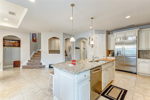 kitchen featuring light stone countertops, a kitchen island with sink, stainless steel appliances, sink, and backsplash