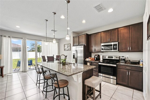 kitchen featuring appliances with stainless steel finishes, an island with sink, light stone countertops, sink, and decorative light fixtures