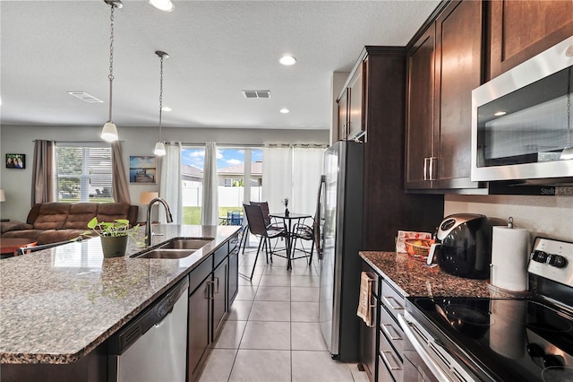 kitchen featuring an island with sink, dark stone countertops, appliances with stainless steel finishes, light tile patterned flooring, and sink