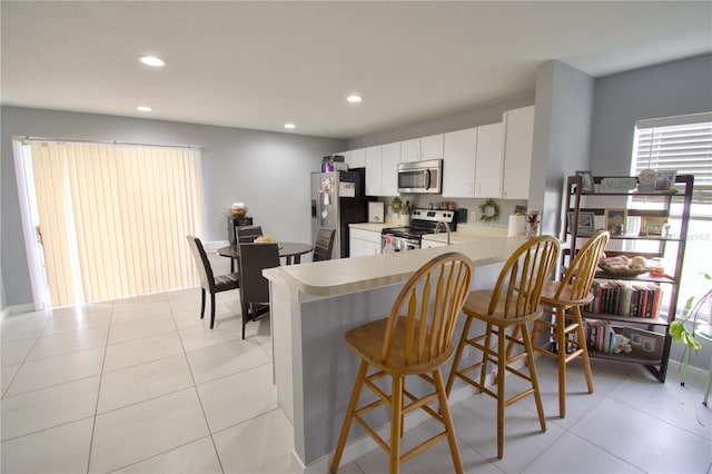 kitchen with a kitchen breakfast bar, kitchen peninsula, white cabinets, light tile patterned floors, and appliances with stainless steel finishes