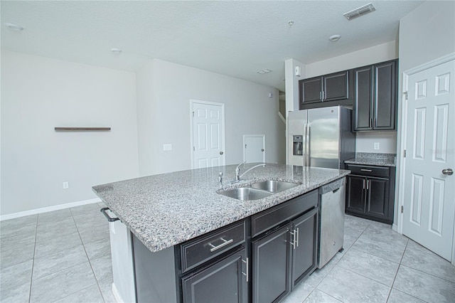 kitchen with stainless steel appliances, a center island with sink, light tile patterned floors, and sink