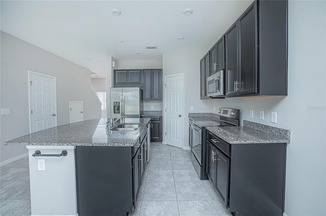 kitchen with light tile patterned flooring, sink, stone counters, a center island with sink, and appliances with stainless steel finishes