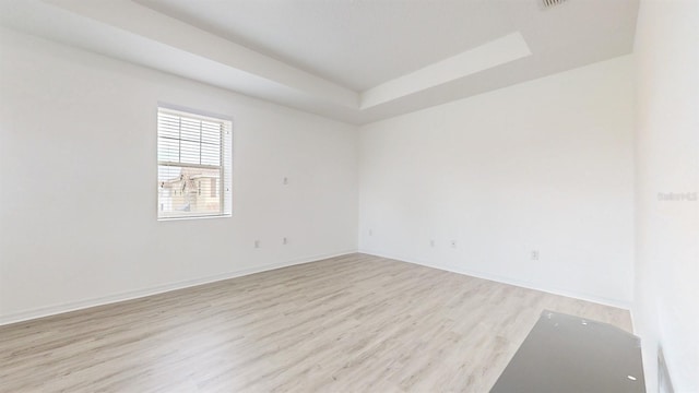 empty room featuring a tray ceiling and light wood-type flooring