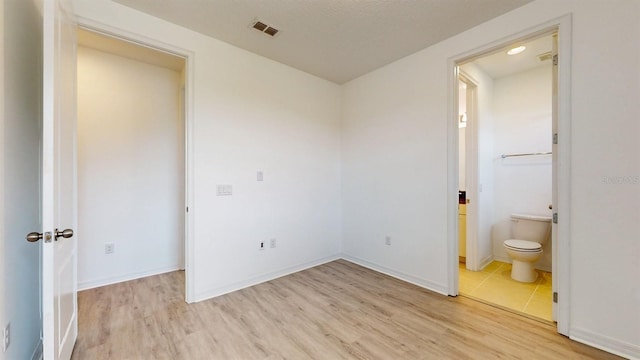 unfurnished bedroom featuring ensuite bath, a textured ceiling, and light wood-type flooring