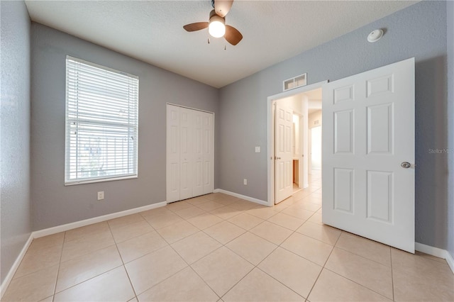 unfurnished bedroom featuring light tile patterned flooring, ceiling fan, a closet, and a textured ceiling