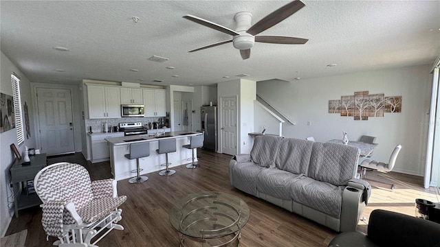 living room with a textured ceiling, dark hardwood / wood-style floors, ceiling fan, and sink