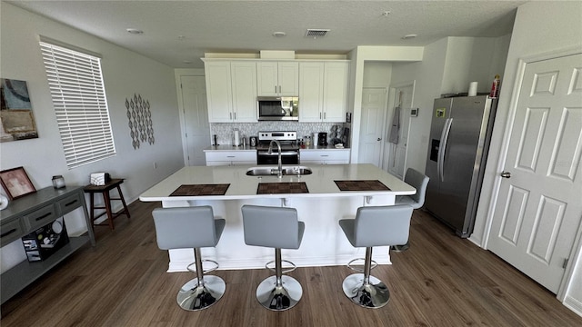 kitchen featuring a kitchen breakfast bar, white cabinetry, stainless steel appliances, a center island with sink, and dark hardwood / wood-style floors