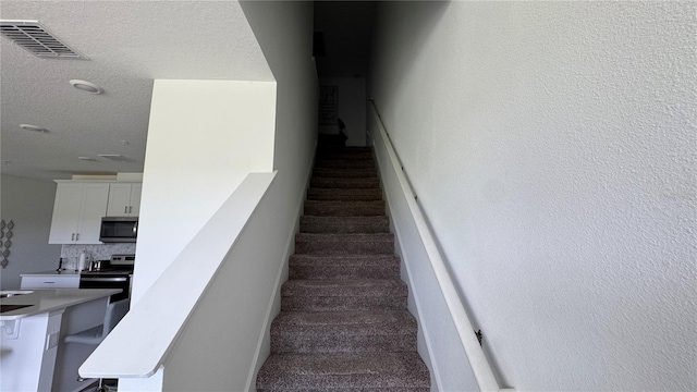 stairway featuring a textured ceiling and carpet floors