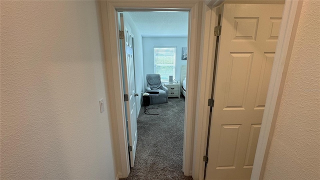 hall with a textured ceiling and dark carpet