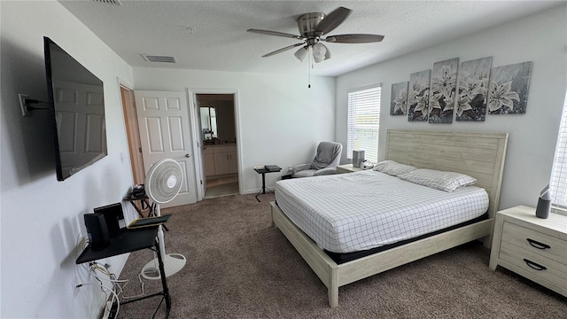 bedroom with a textured ceiling, connected bathroom, dark carpet, and ceiling fan