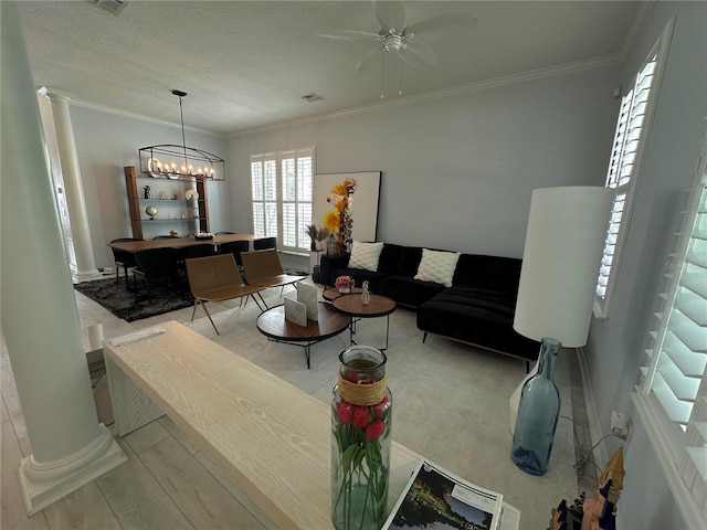 living room with ornamental molding, a textured ceiling, ceiling fan with notable chandelier, and decorative columns