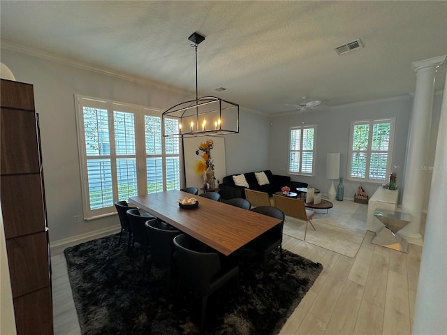 dining area with a textured ceiling, light hardwood / wood-style flooring, ceiling fan with notable chandelier, crown molding, and ornate columns