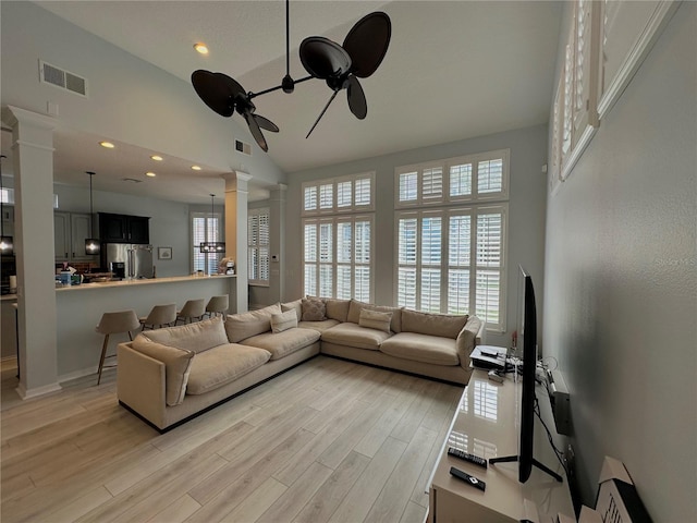 living room with high vaulted ceiling, decorative columns, ceiling fan, and light wood-type flooring