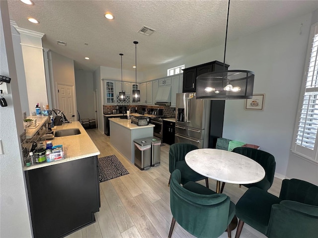 kitchen with tasteful backsplash, a textured ceiling, a kitchen island with sink, light hardwood / wood-style flooring, and appliances with stainless steel finishes