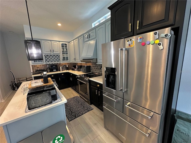 kitchen featuring custom exhaust hood, hanging light fixtures, light hardwood / wood-style flooring, backsplash, and stainless steel appliances