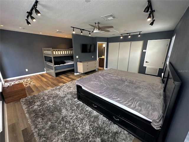 bedroom with a closet, a textured ceiling, track lighting, hardwood / wood-style flooring, and ceiling fan