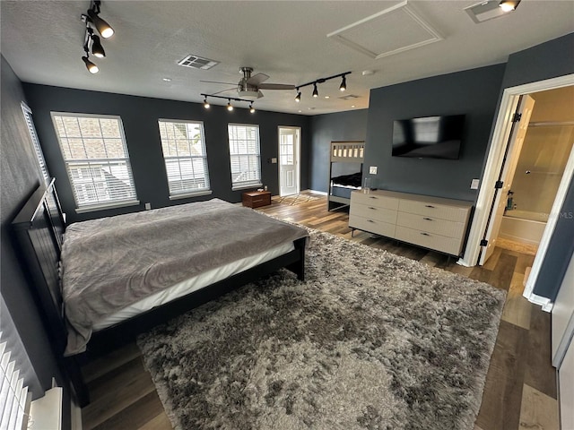 bedroom with a textured ceiling, ensuite bathroom, dark wood-type flooring, and rail lighting