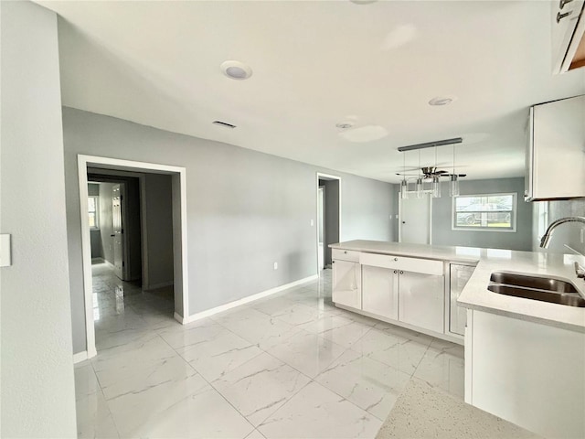 kitchen featuring sink, kitchen peninsula, white cabinets, and decorative light fixtures