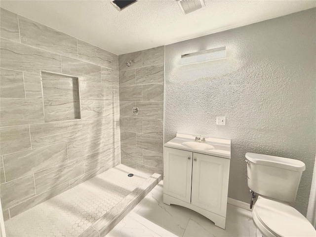 bathroom with vanity, a tile shower, a textured ceiling, and toilet