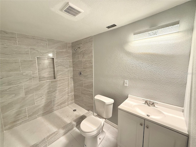 bathroom featuring vanity, tiled shower, a textured ceiling, and toilet