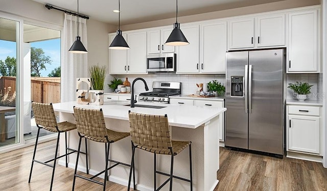 kitchen with white cabinetry, backsplash, stainless steel appliances, wood-type flooring, and a kitchen island with sink